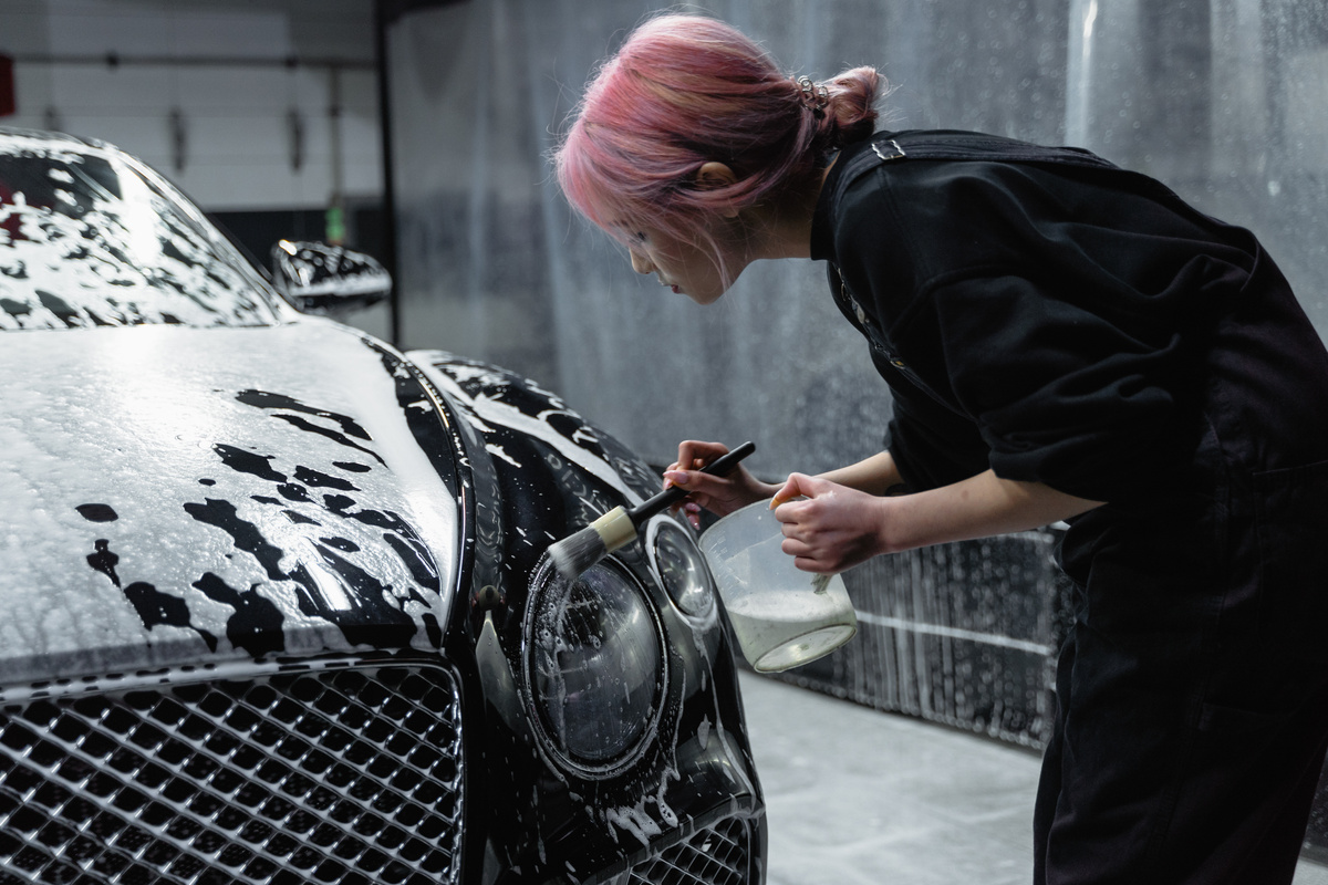 Photo of a Woman with Pink Hair Brushing the Headlight of a Black Car
